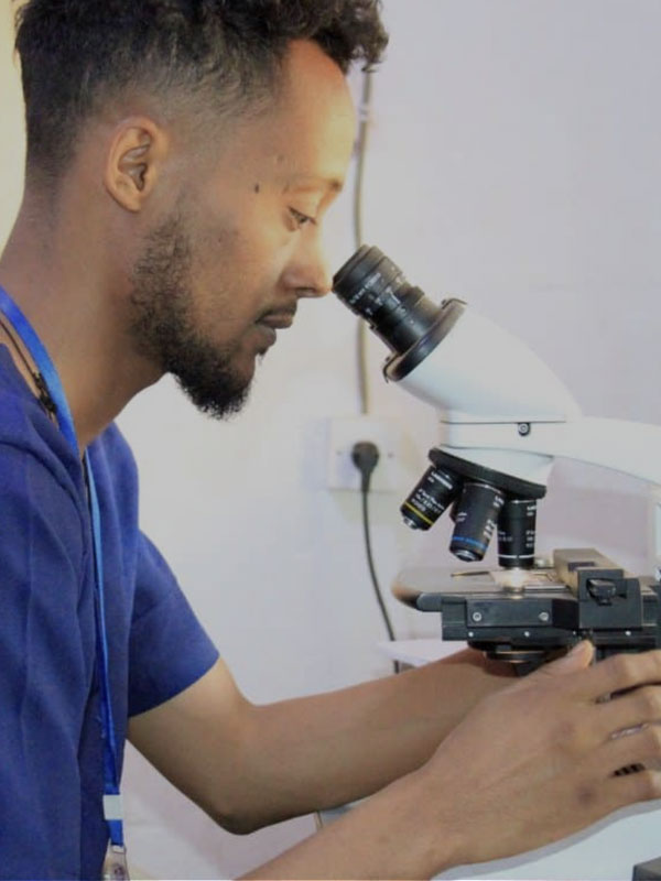 A lab technician looking through a microscope.