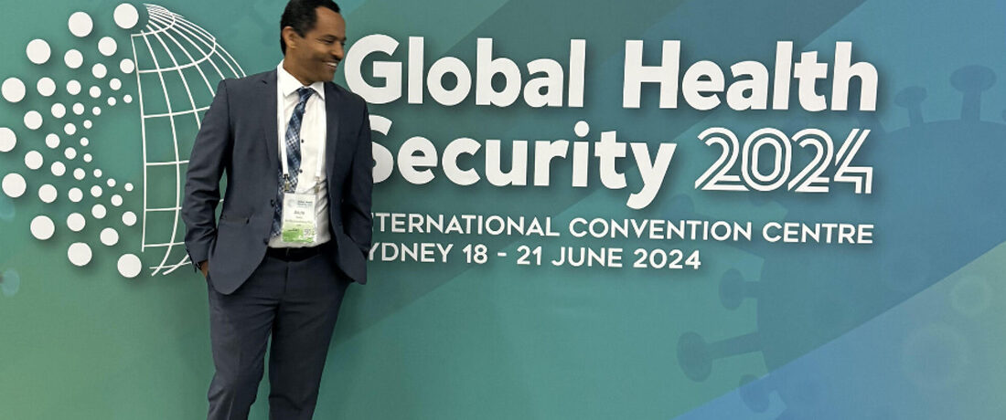 Dr. Alula Teklu posing for photo in front of Global Health Security banner