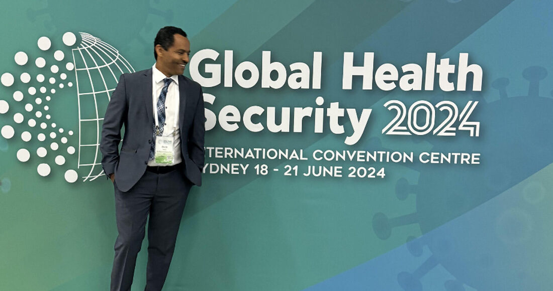 Dr. Alula Teklu posing for photo in front of Global Health Security banner