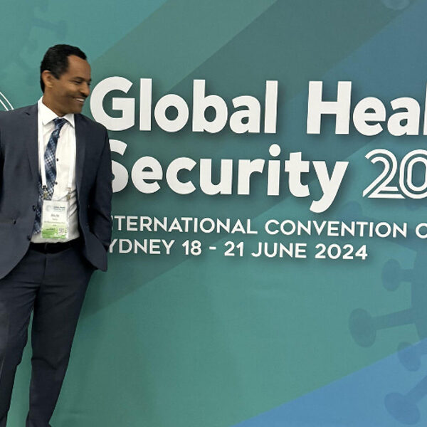 Dr. Alula Teklu posing for photo in front of Global Health Security banner