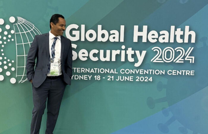 Dr. Alula Teklu posing for photo in front of Global Health Security banner